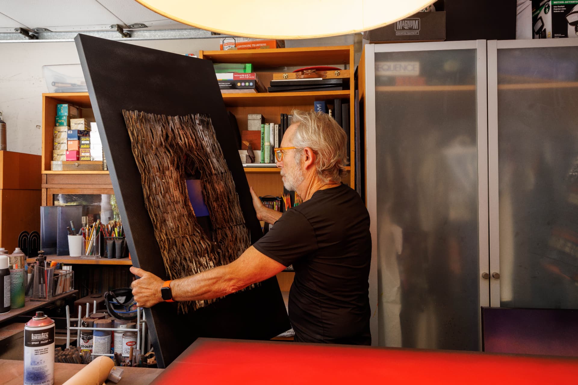 Jorge Engel holding a textured mixed-media work in his studio